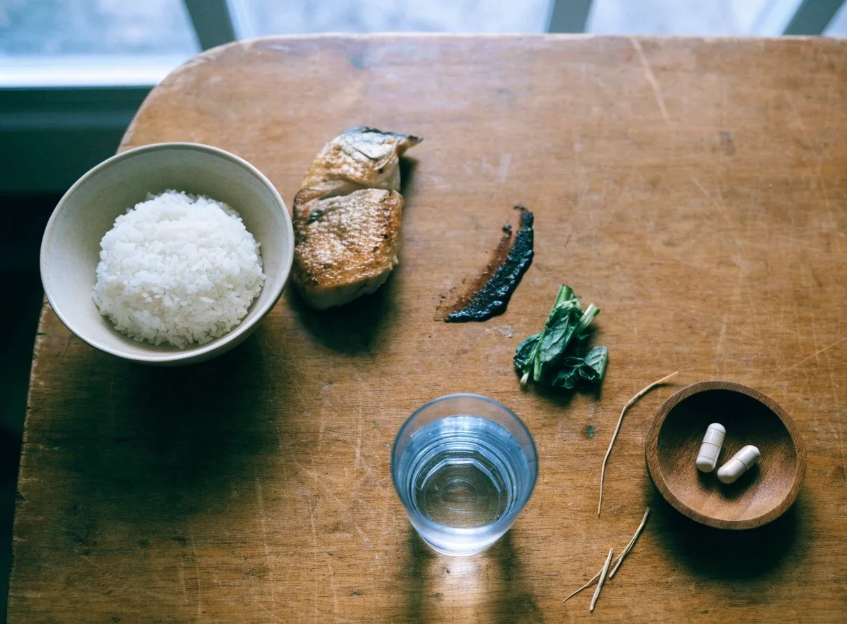 A simple midday meal with rice, fish, greens and a wooden dish holding daily capsules